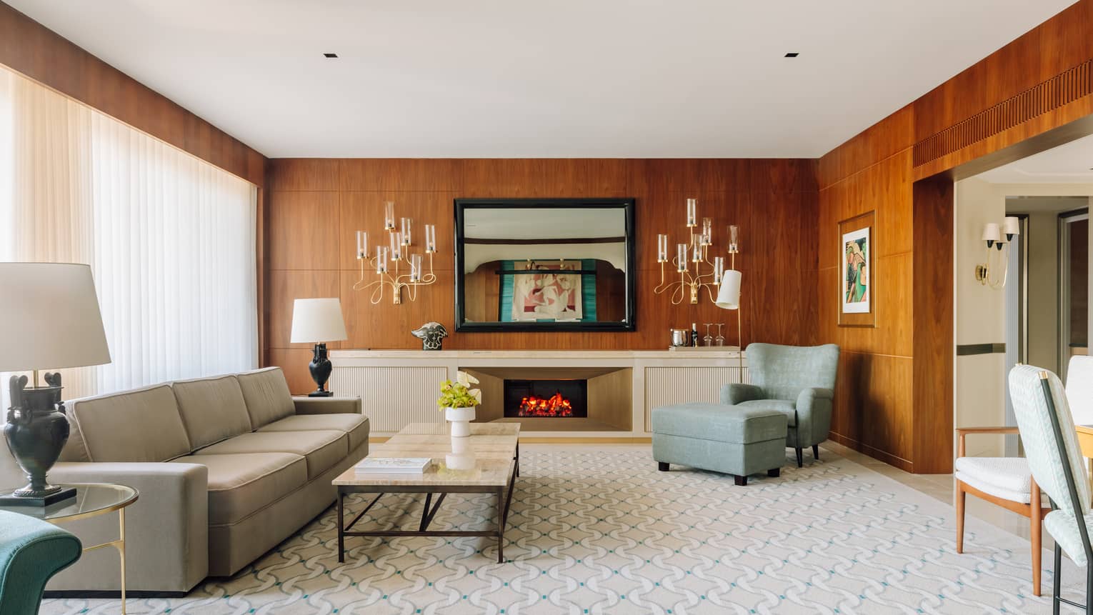 Spacious hotel living room with a sofa, armchair, fireplace, coffee table and wood-paneled walls with decorative lighting.