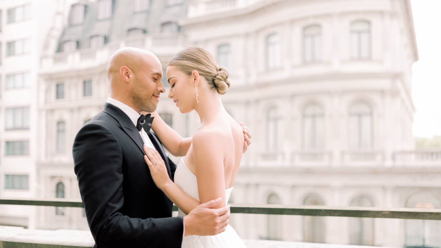 A tender moment captured on the balcony of the Four Seasons London Park Lane in Mayfair, featuring a bride and groom in an intimate embrace on their wedding day. The bride, dressed in an elegant strapless gown, and the groom, in a classic black tuxedo, are gently holding each other while gazing into each other's eyes. The soft focus background showcases the grand architecture of Mayfair, adding a romantic and luxurious atmosphere to this special occasion.,A tender moment captured on the balcony of Four Seasons London Park Lane in Mayfair, featuring a bride and groom in an intimate embrace on their wedding day. The bride, dressed in an elegant strapless gown, and the groom, in a classic black tuxedo, are gently holding each other while gazing into each other's eyes. The soft focus background showcases the grand architecture of Mayfair, adding a romantic and luxurious atmosphere to this special occasion.