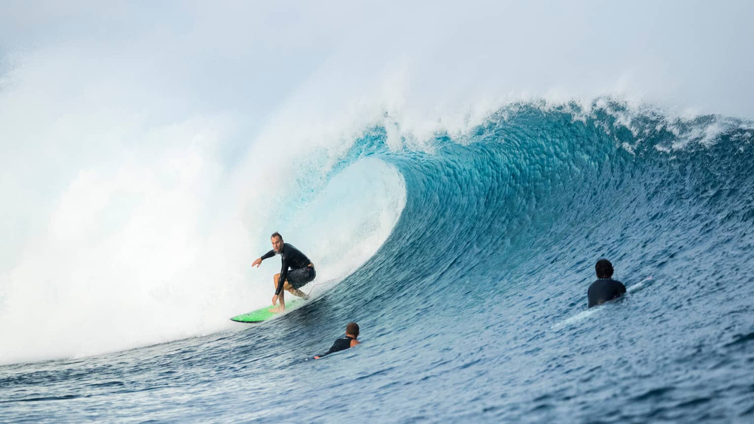 Surfer rides surfboard on large wave, two surfers swimming in water