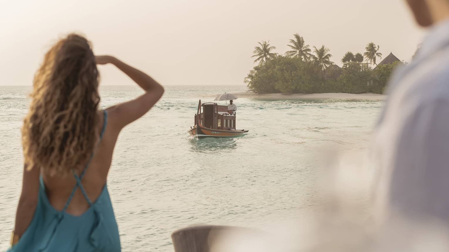 Person in blue dress shields eyes as boat travels toward shore