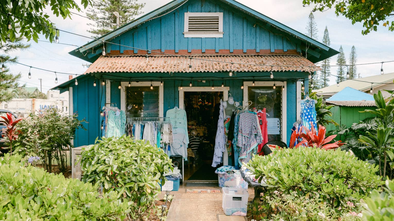 A shop in a small bright turquoise house surrounded by greenery