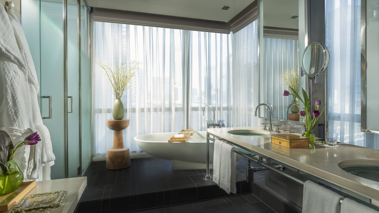 Luxurious bathroom with a freestanding bathtub, double-sink vanity and floor-to-ceiling windows with curtains, decorated with flowers