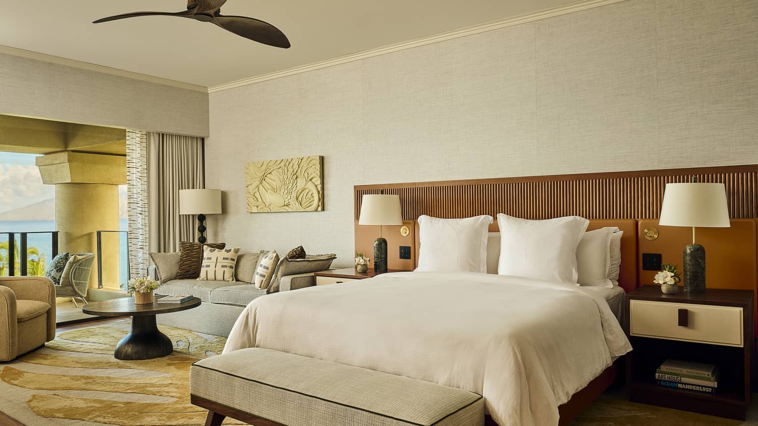 Luxury resort suite bedroom with king bed, wooden headboard wall, sitting area and ocean-view balcony