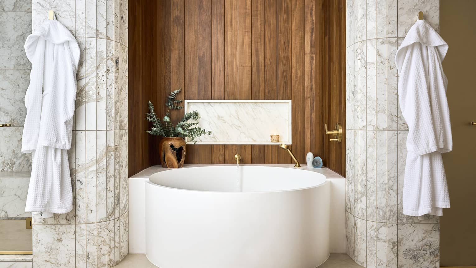 Luxury resort suite bathroom with large standalone, circular tub in between two marble pillars