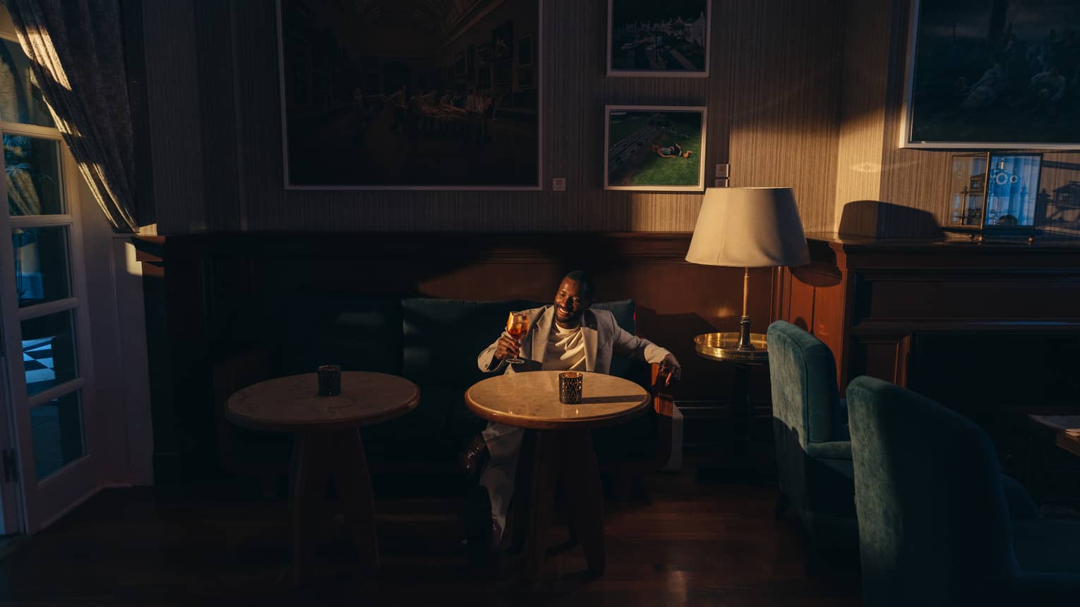 A person holding a drink sits at a table in a bar