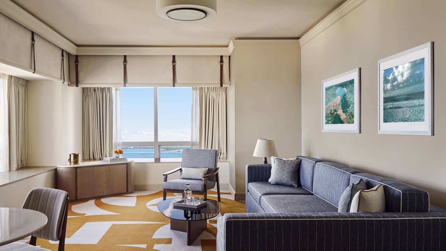 Hotel suite living room with dark grey-blue sofa, orange and white carpet, arm chair and window with bay view
