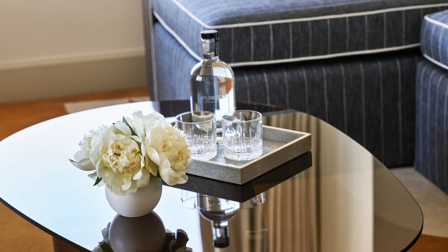 Close-up of a coffee table with flowers and a bar tray holding two crystal glasses and bottle of water