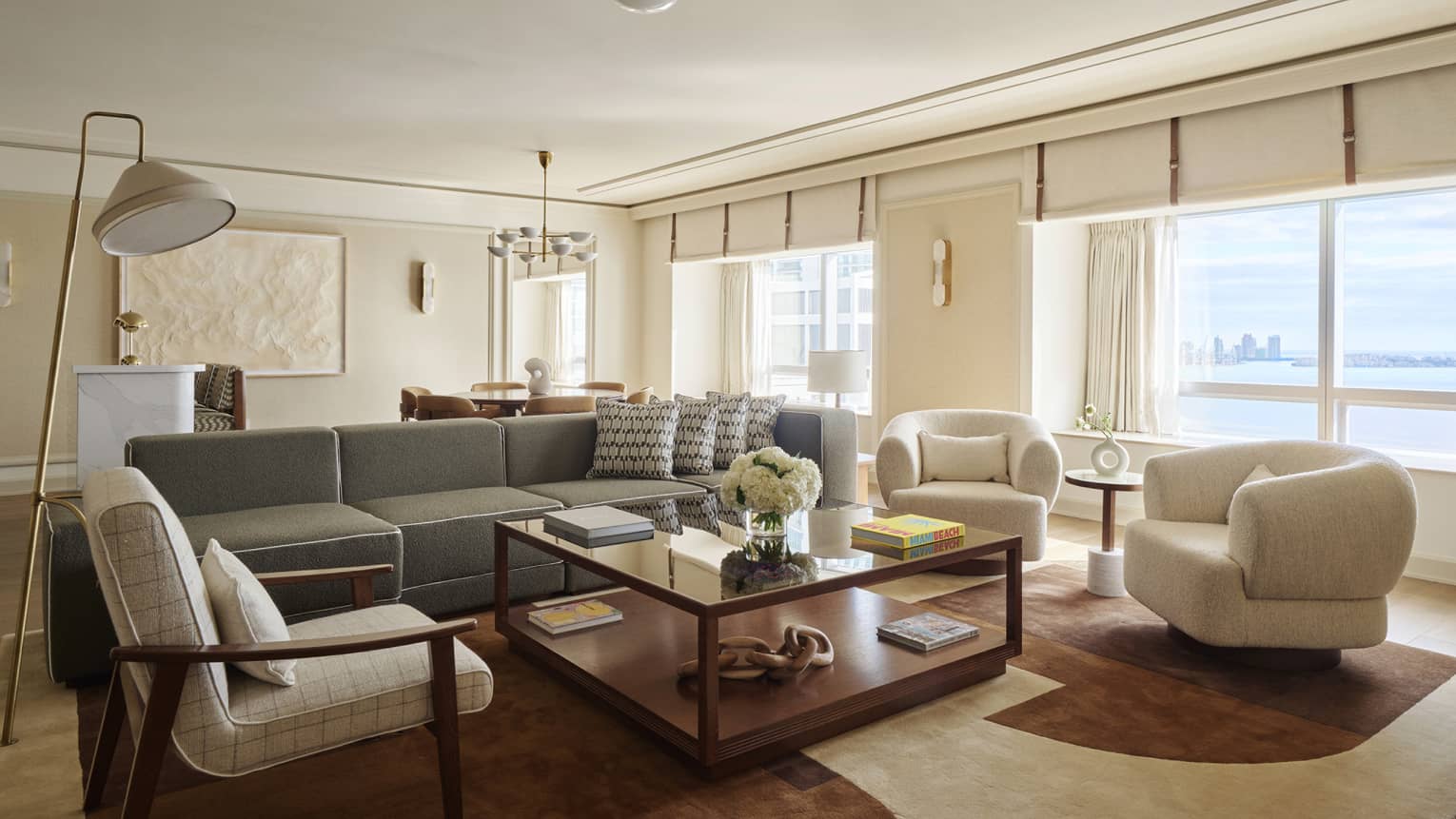 Mid-century modern living room with sofa and three arm chairs surrounding a large square coffee table, and large picture windows overlooking bay