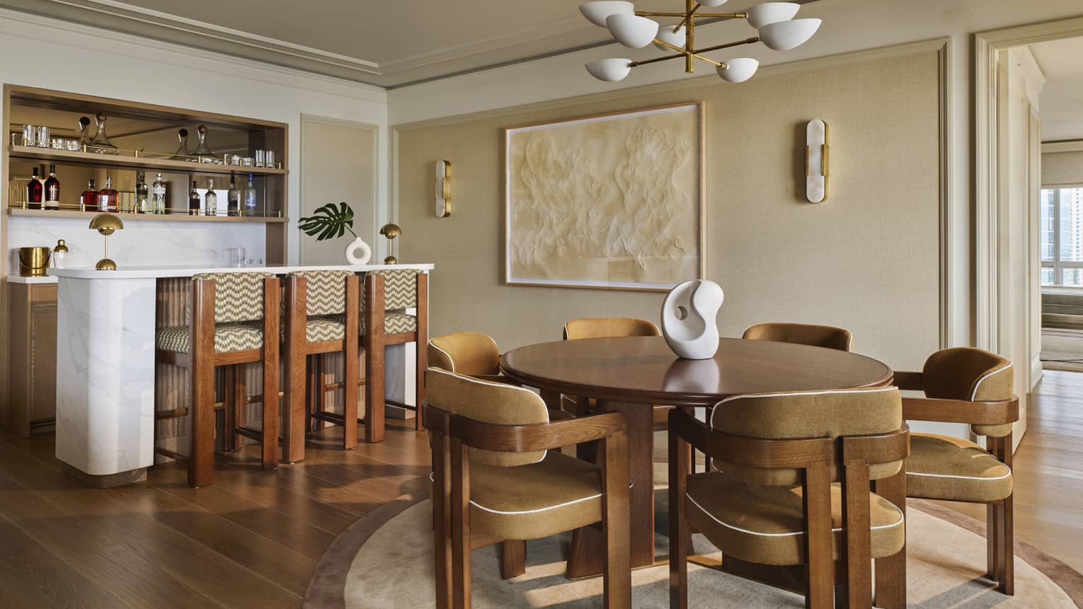 A hotel suite's kitchen with bar counter and dining area with round wooden table, six chairs and