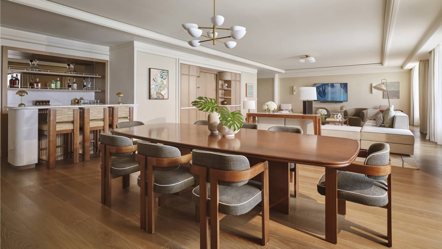 A hotel suite's dining room with wooden floors, wooden dining table with eight chairs and an open floor plan into the living room and kitchen