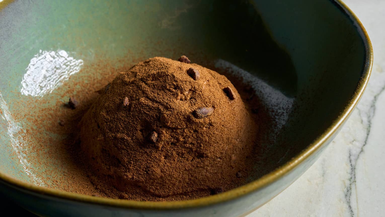 A green bowl with a cacao dessert topped with chocolate chips
