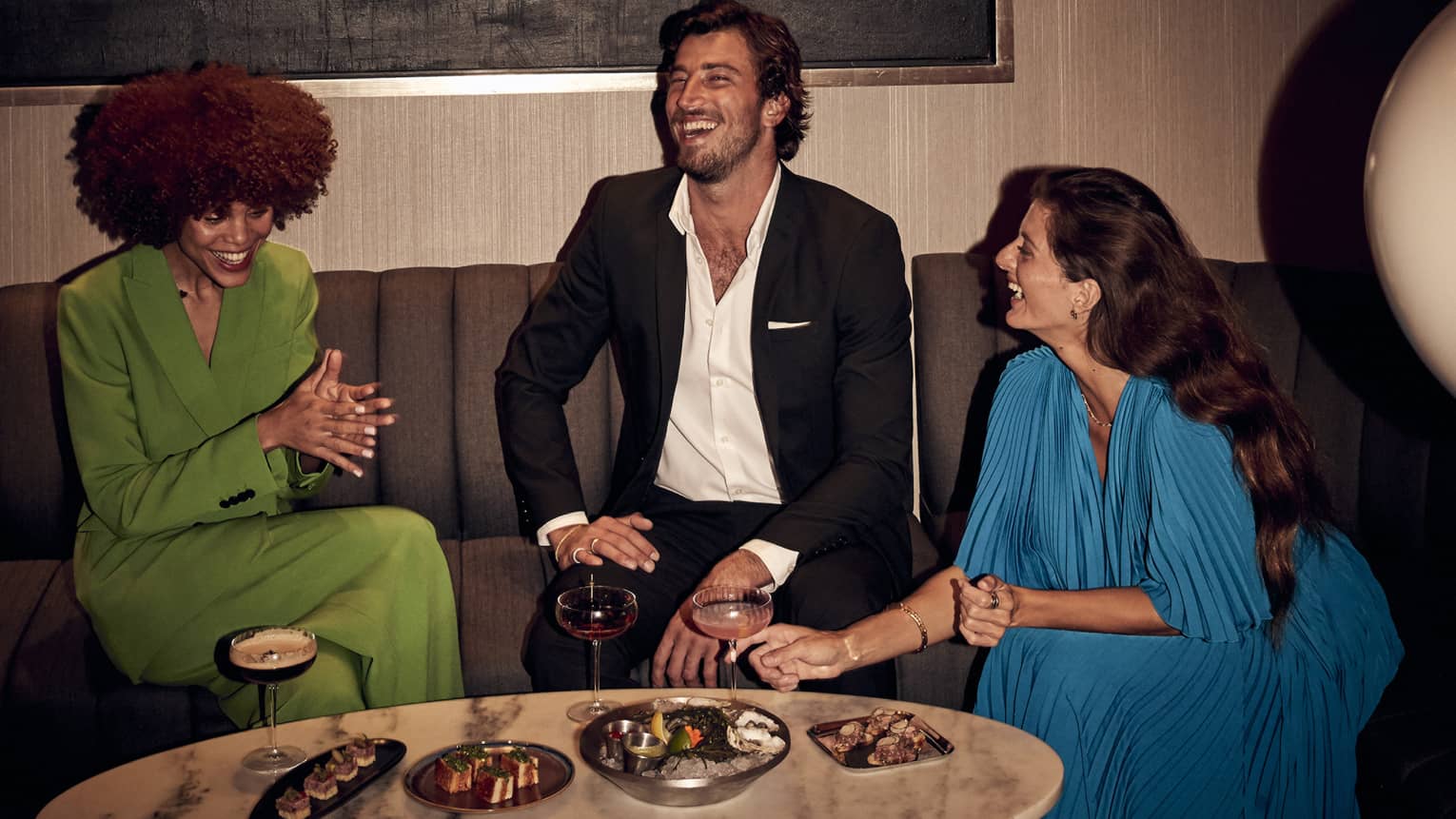 Two women and one man life around lounge coffee table with small plates