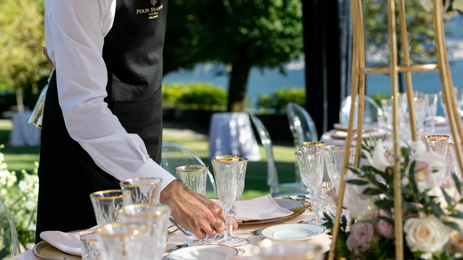 Wedding reception, hotel staff places gold rimmed wine glass on outdoor dining table