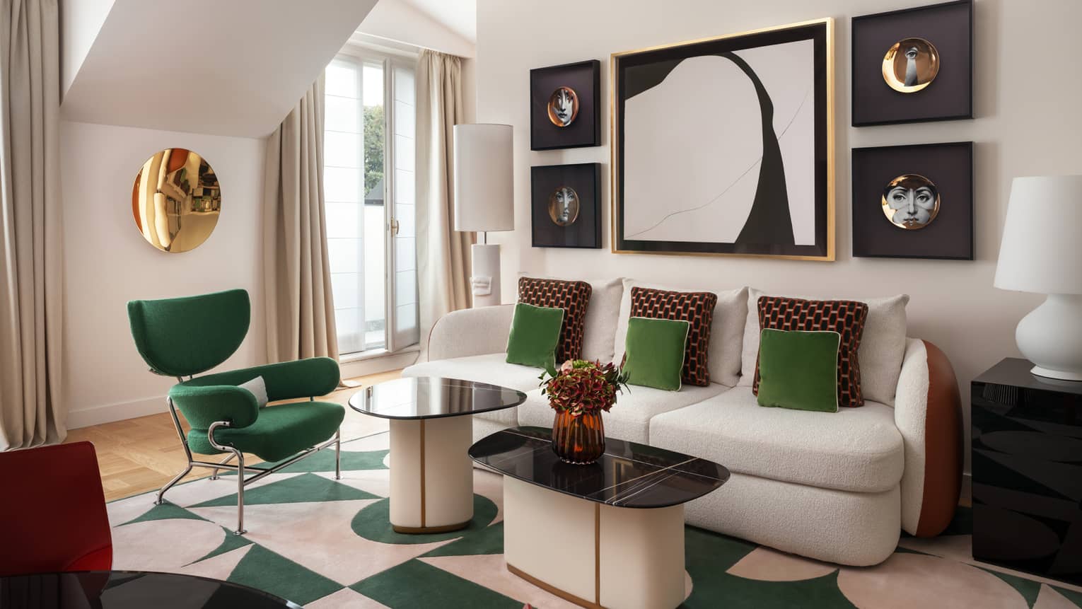Contemporary hotel suite living room, featuring a sofa with emerald-green and burgundy throw pillows, a green arm chair, and abstract artwork on the wall