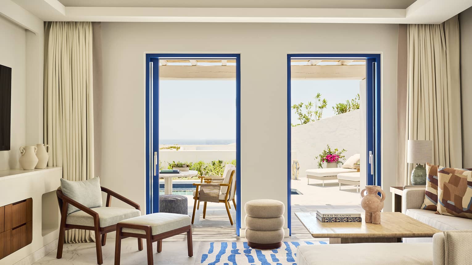 Greek-inspired luxury resort room featuring a living room with a sofa and arm chair, as well as a walk-out sea-view terrace