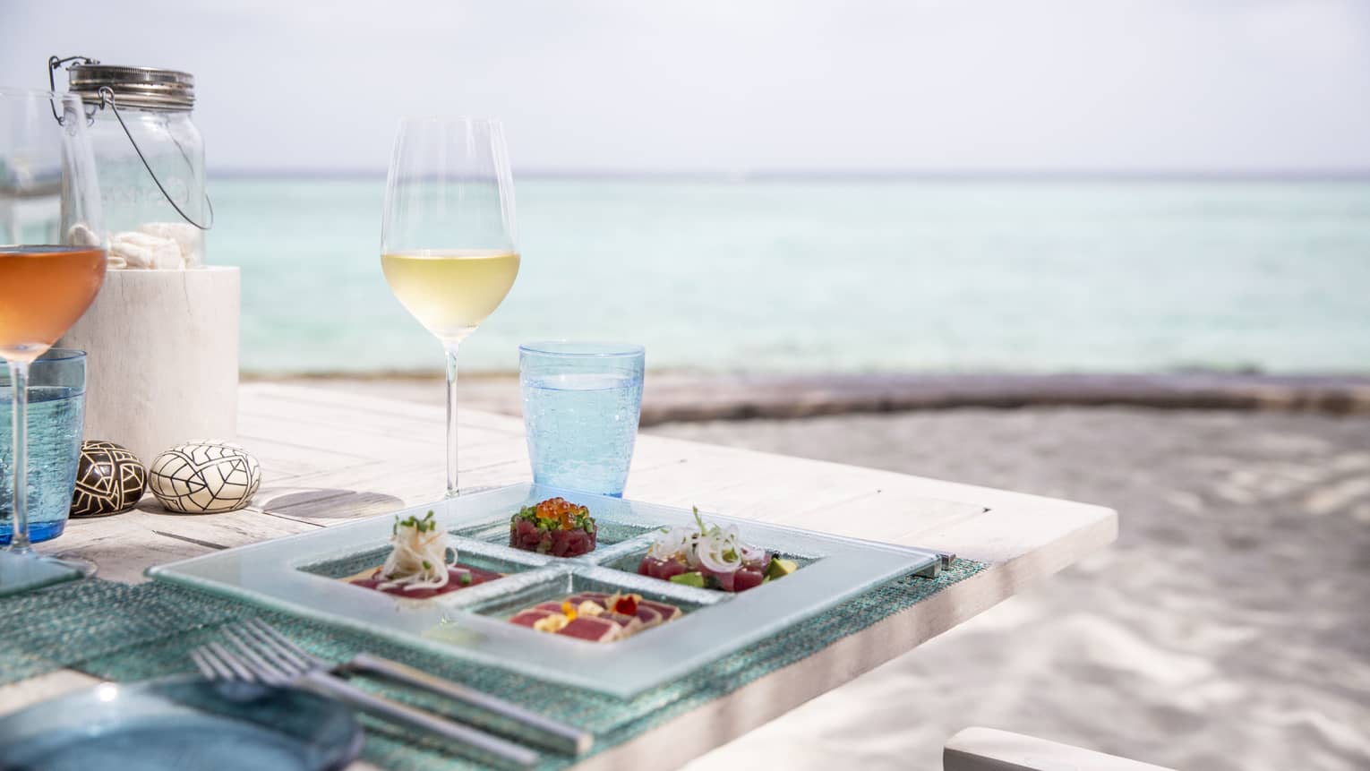 A tasetfully set table with a glass of white wine and rose overlooking the ocean at Fuego Grill