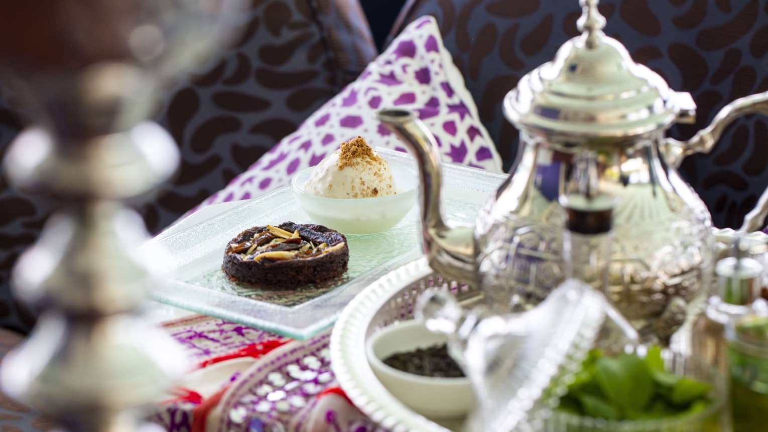 A sterling silver teapot and light tea time finger foods sit on a decorative table spread atAl Barakat