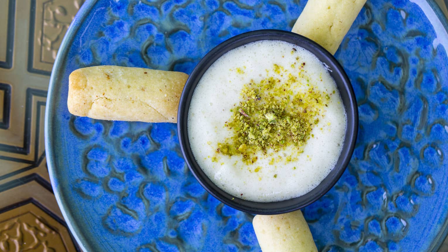 An overhead view of a white sauce with spices sprinkled on top and bread sticks around it, on a blue pottery dish