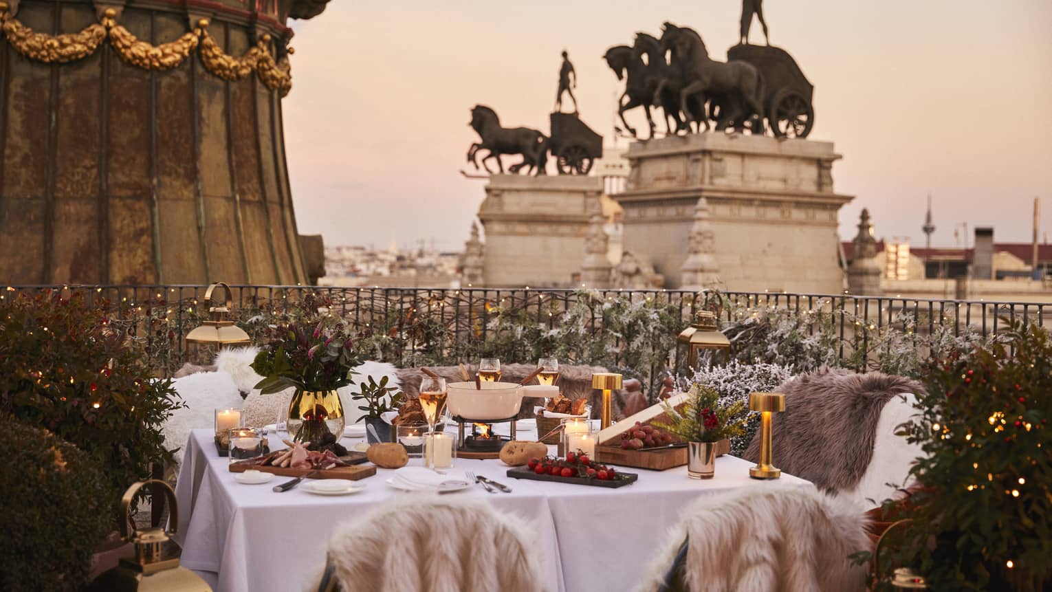 Terrace with table set with winter d�cor and fur throws, overlooking tall statues at dusk