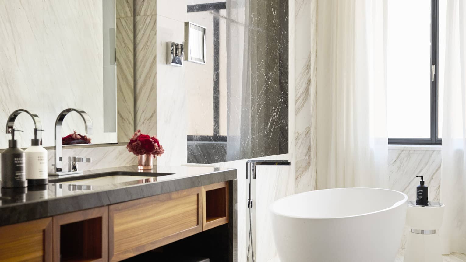Sleek hotel room bathroom with free-standing oval bath tub next to window
