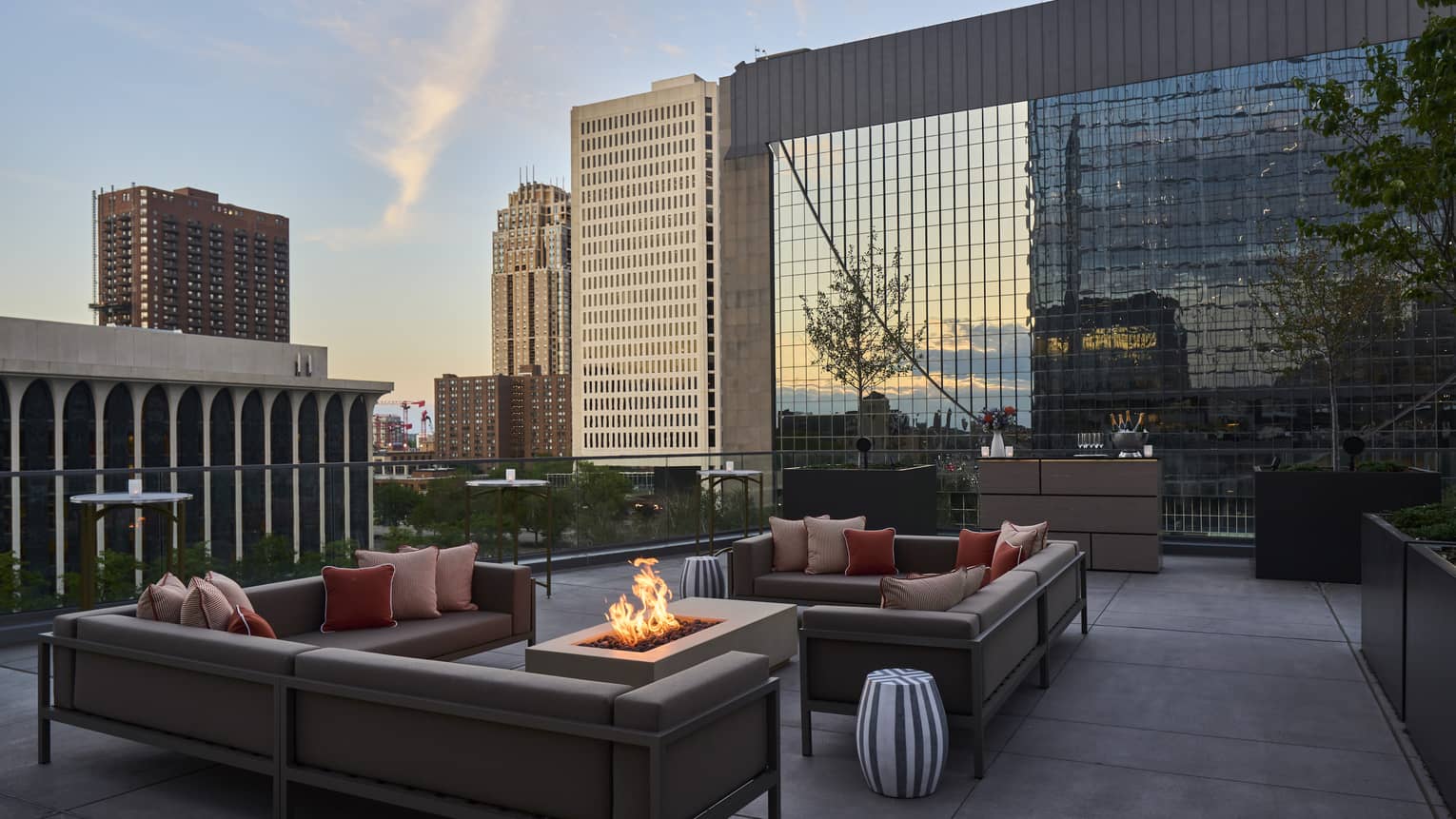 A seating area on a terrace with a fire pit, couches and small tables.