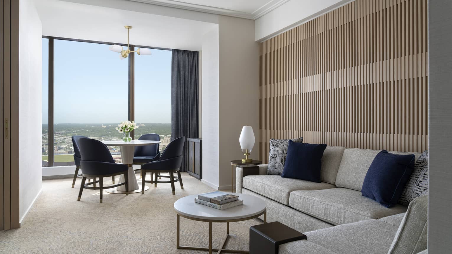 Living room with grey sofas, modern wood paneled wall, round dining table for four, wall of windows with city view