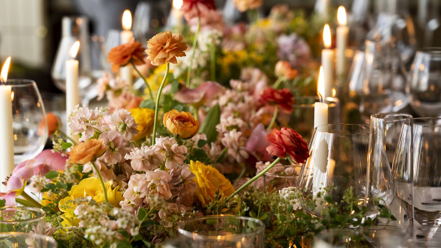 Table setting with candles and orange, red and pink flowers.