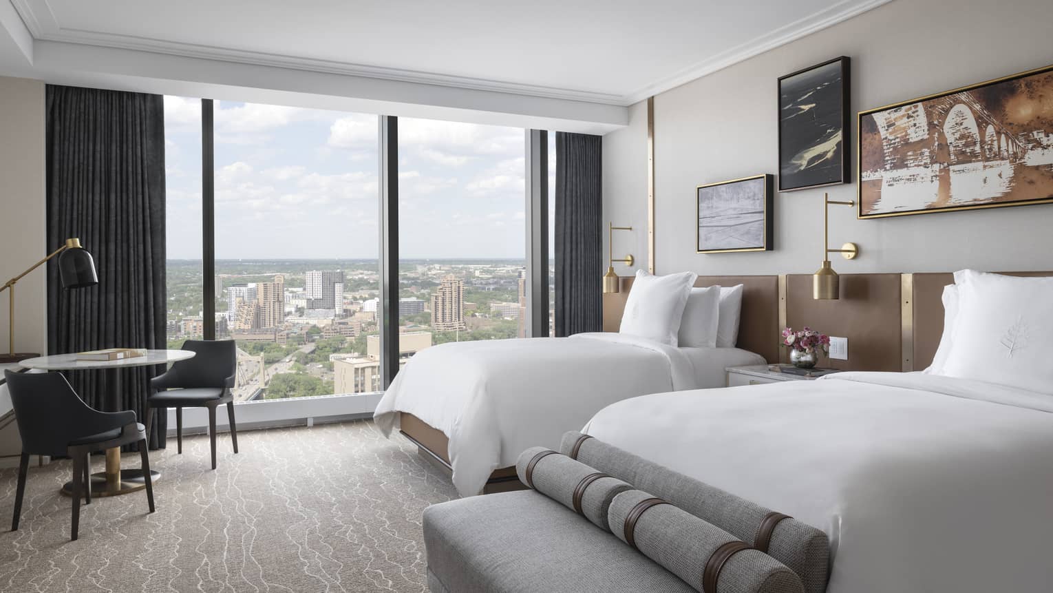 Hotel room with two double beds, table and two chairs, grey bench and window