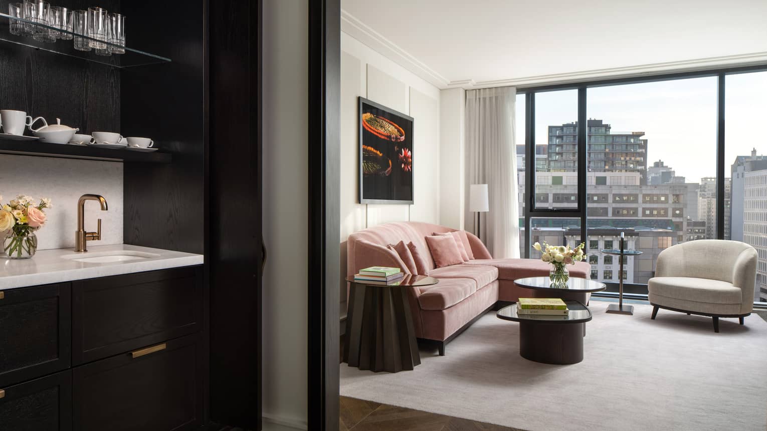 Hotel room living area with pink velvet sofa, ivory arm chair and wall of windows