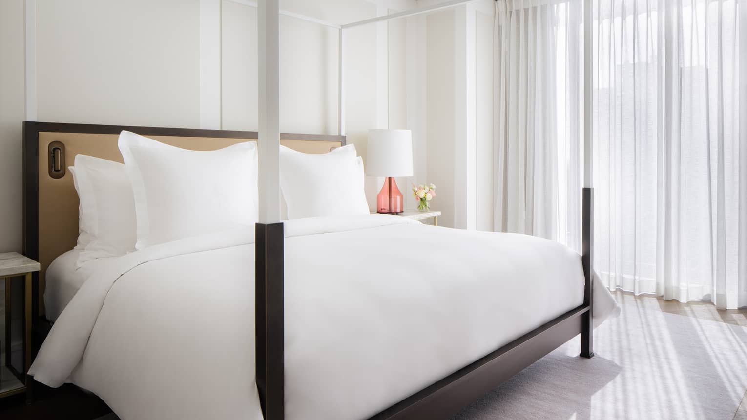 Modern, four-poster king bed with white sheets