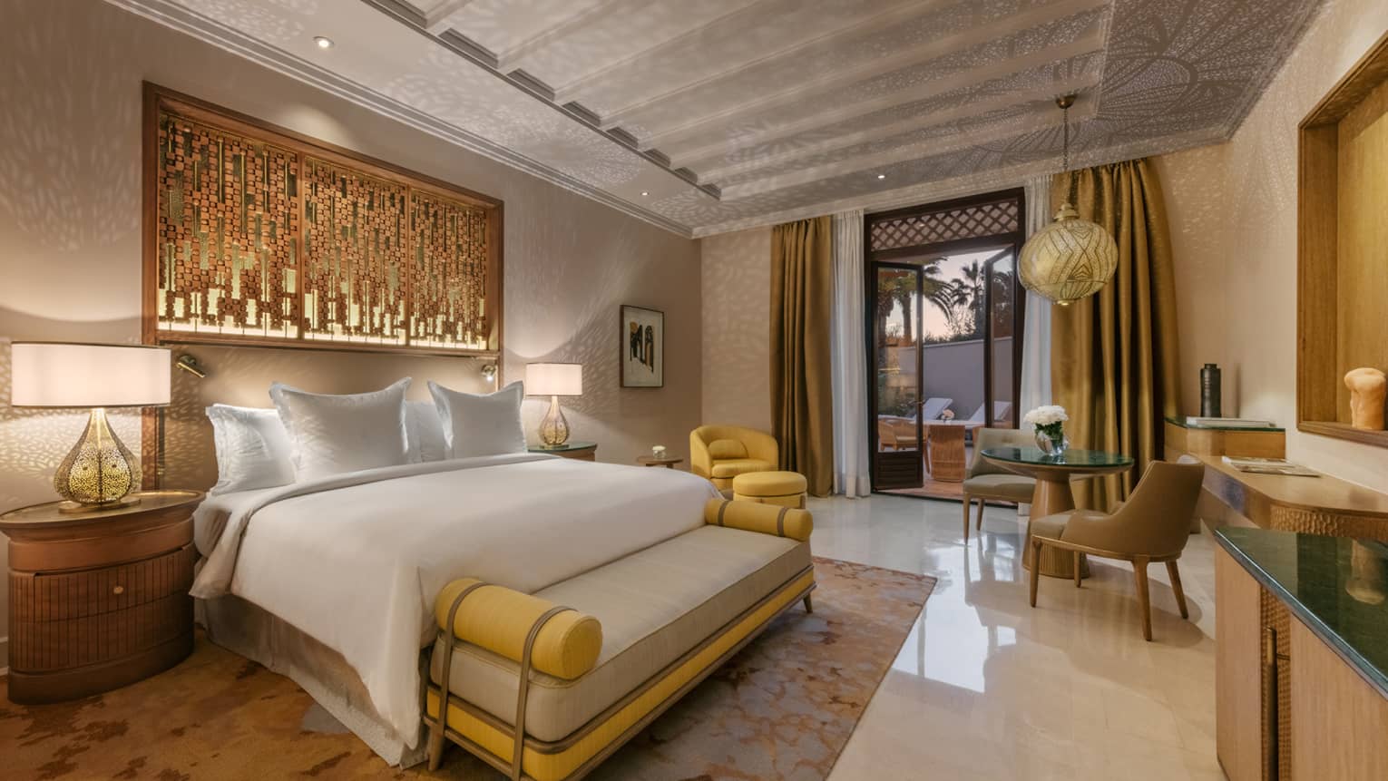 Marrakech hotel room with king bed, cushioned bench, yellow and bronze accents