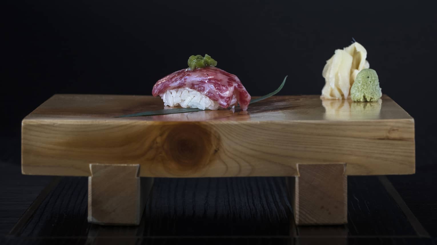 Wood board with piece of sushi topped with raw fish, wasabi