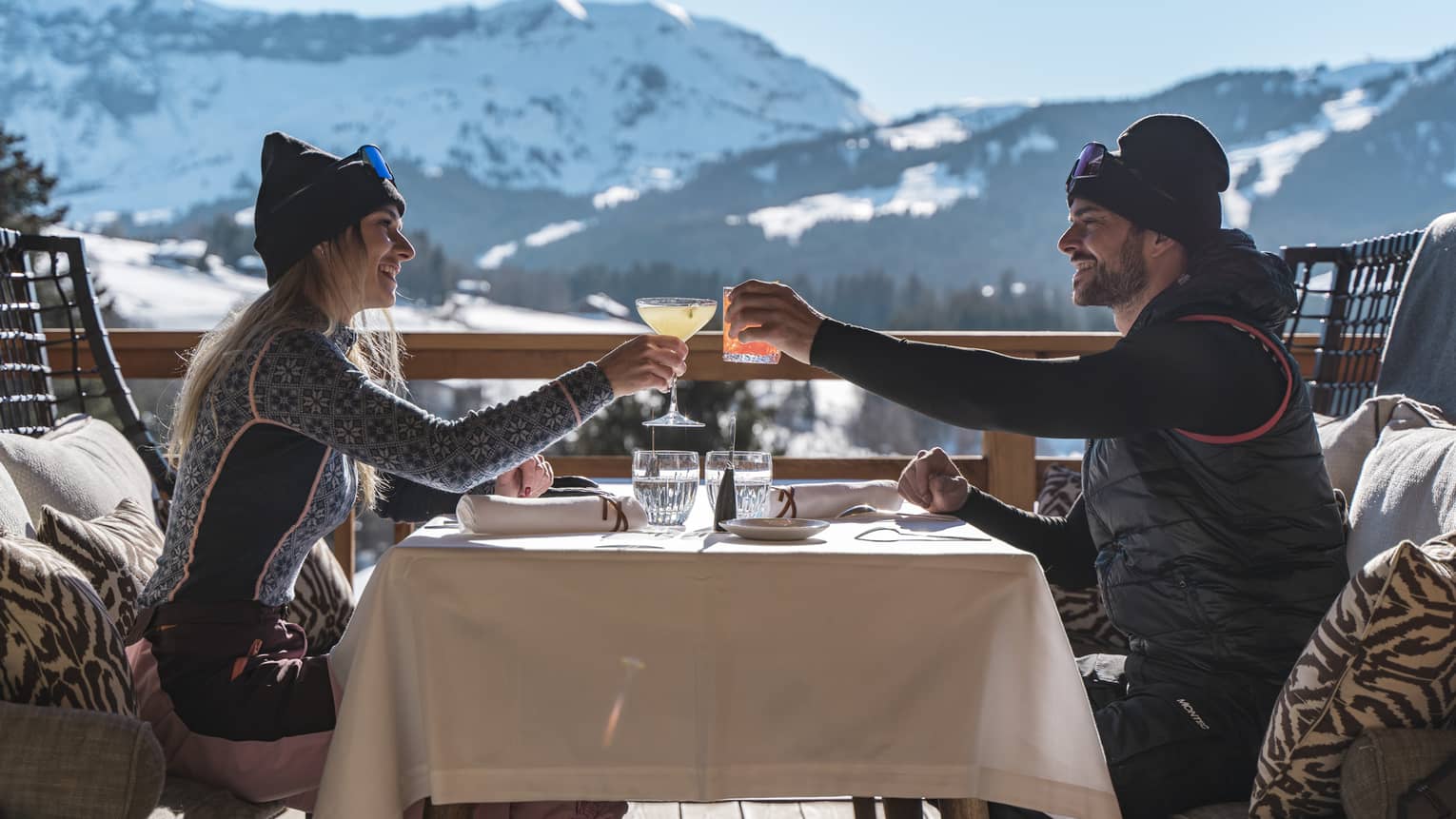 Two people drinking on a patio outside with snowy mountains in the distance