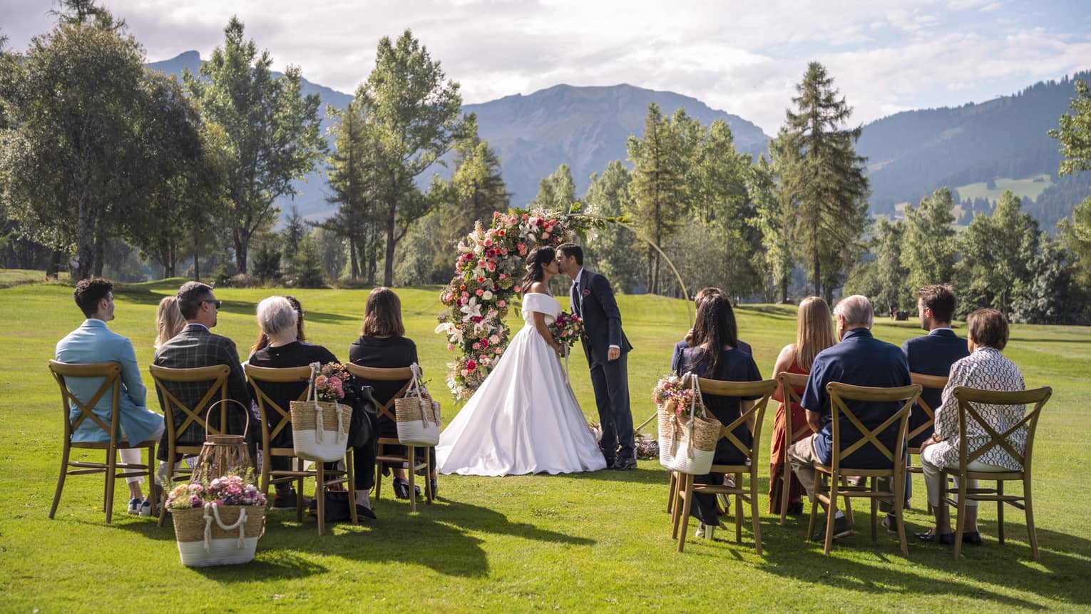 Bridal couple kissing at outdoor wedding in front of intimate group with French Alps in backdrop