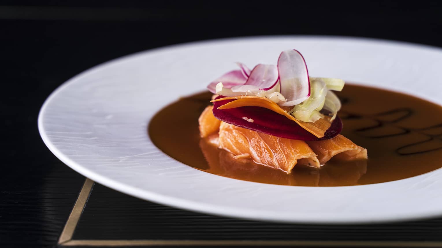 Salmon Tataki garnished with a beetroot slice, shaved carrot ribbon, and ginger and radish slices