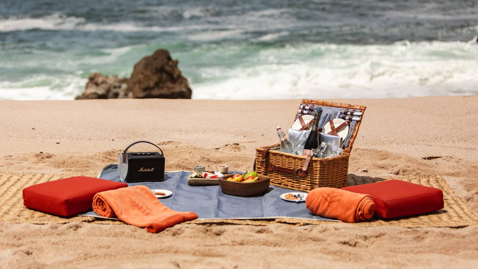 A picnic basket with cushions and a blanket on a beach.