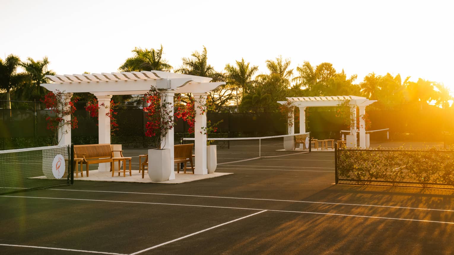Three tennis courts with a white pergola and seating set between each court