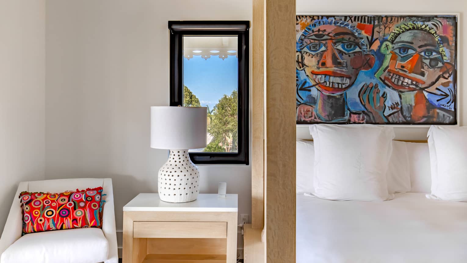 Bedroom with canopy bed, modern artwork overhead and armchair next to side table, sea-view window