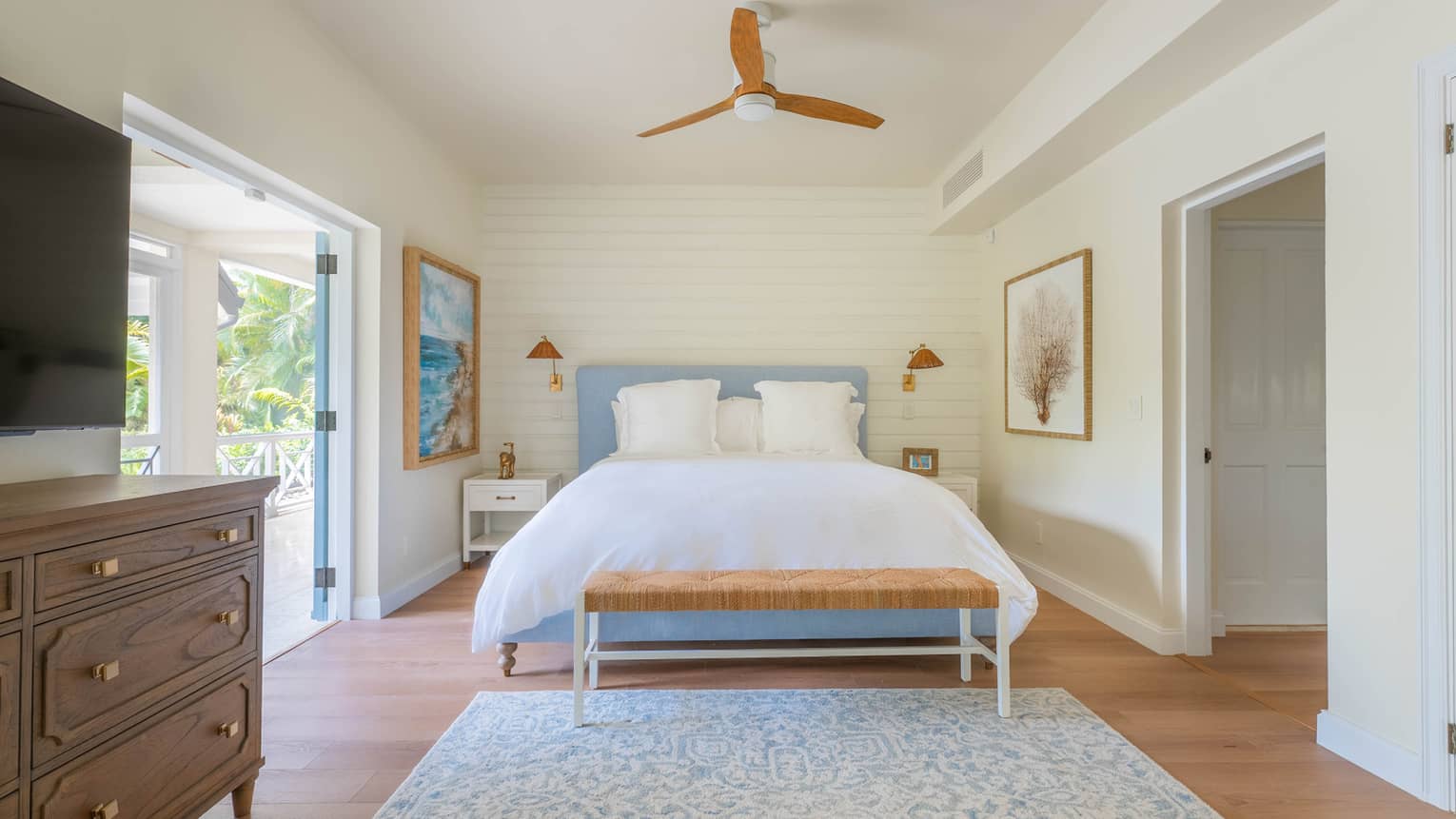 Bedroom with king bed, blue headboard, blue and white rug, dresser, TV, ceiling fan and walk-out terrace