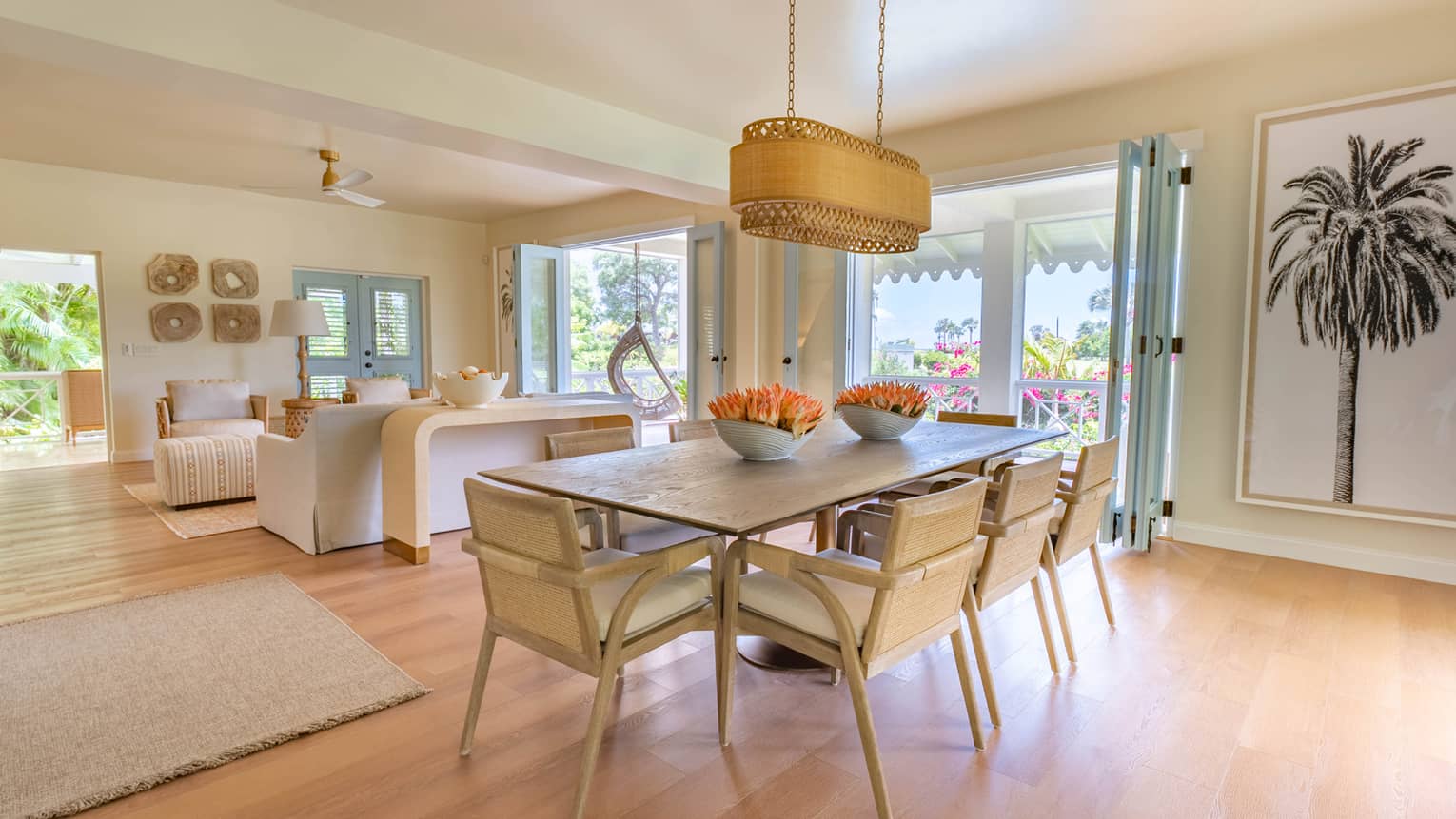 Dining room table with eight chairs, modern rattan lighting fixture, palm tree artwork, wooden floors and walk-out terrace