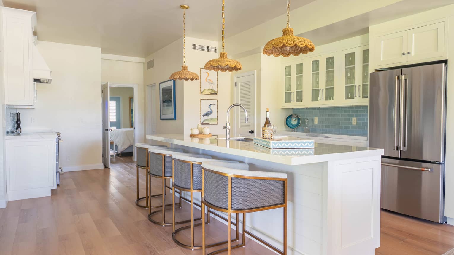 White kitchen featuring stainless steel fridge and an island with four brass and grey upholstered counter-height chairs,
