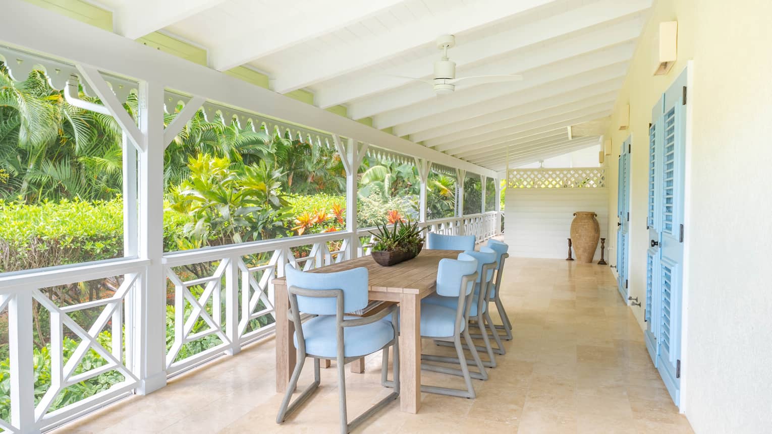 Covered outdoor terrace featuring a dining table with eight blue chairs, set next to garden setting