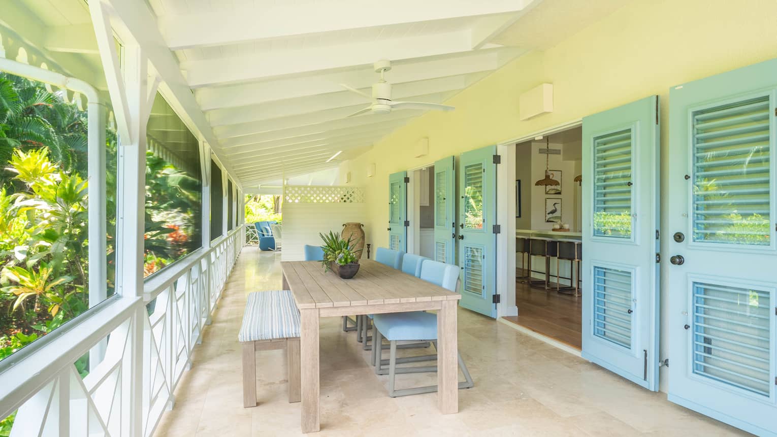 Covered outdoor terrace of a private residence, featuring light blue shuttered doors, and a dining table