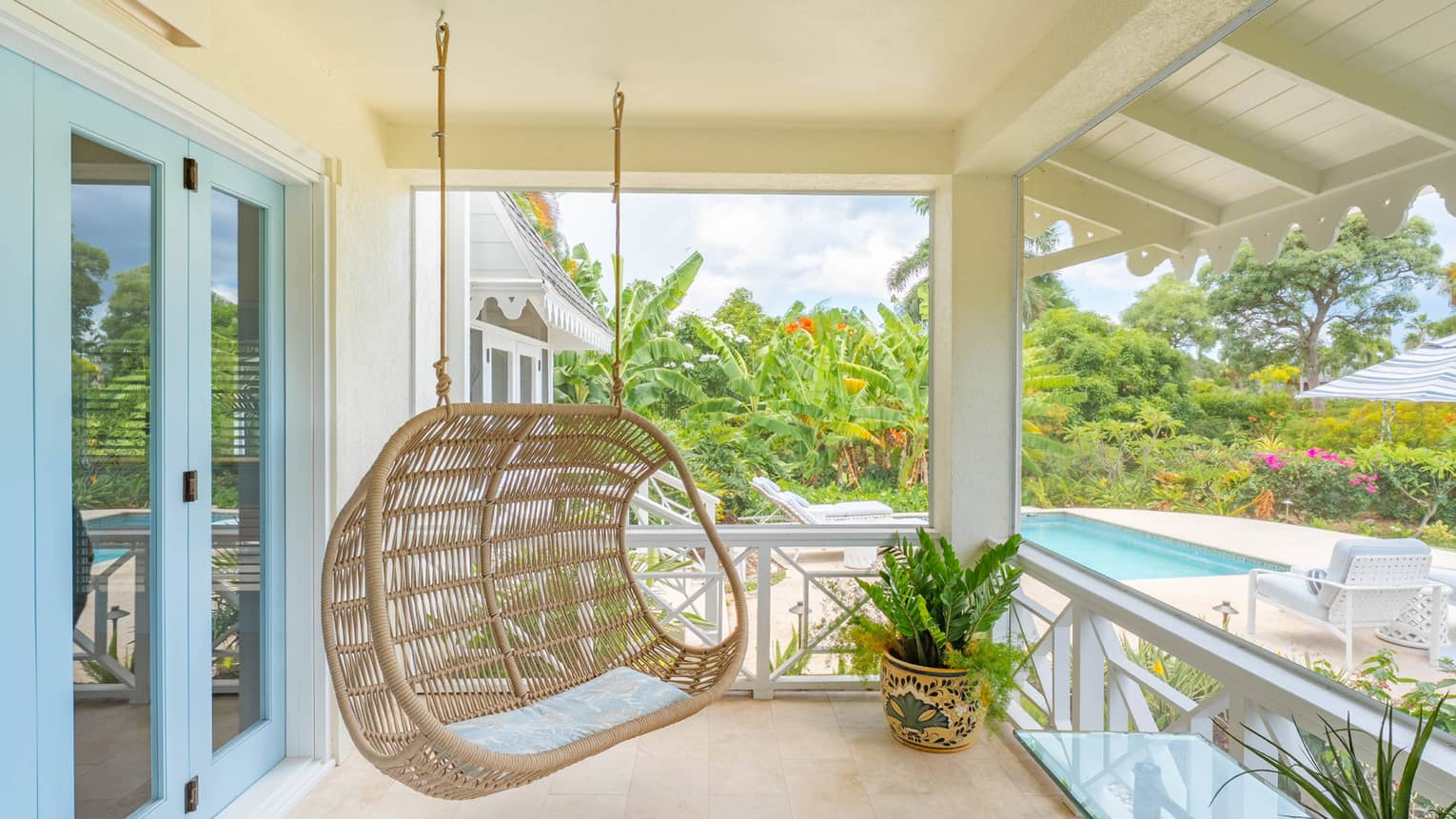 Covered outdoor terrace of a tropical residence, featuring a hanging rattan chair