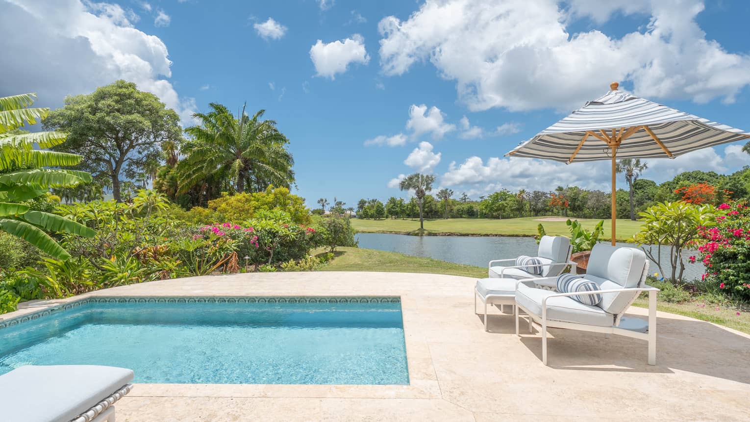 Square pool, two arm chairs under a striped umbrella, and a pond in the background