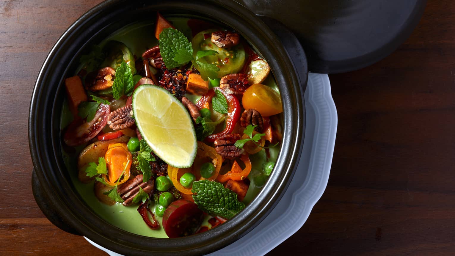 Green curry with herbs and vegetables in a black bowl.