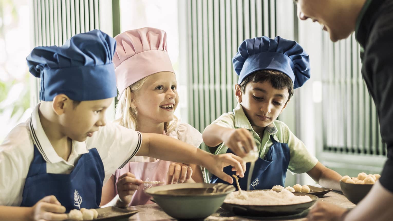 Three children with pink or blue chefs hats making food.