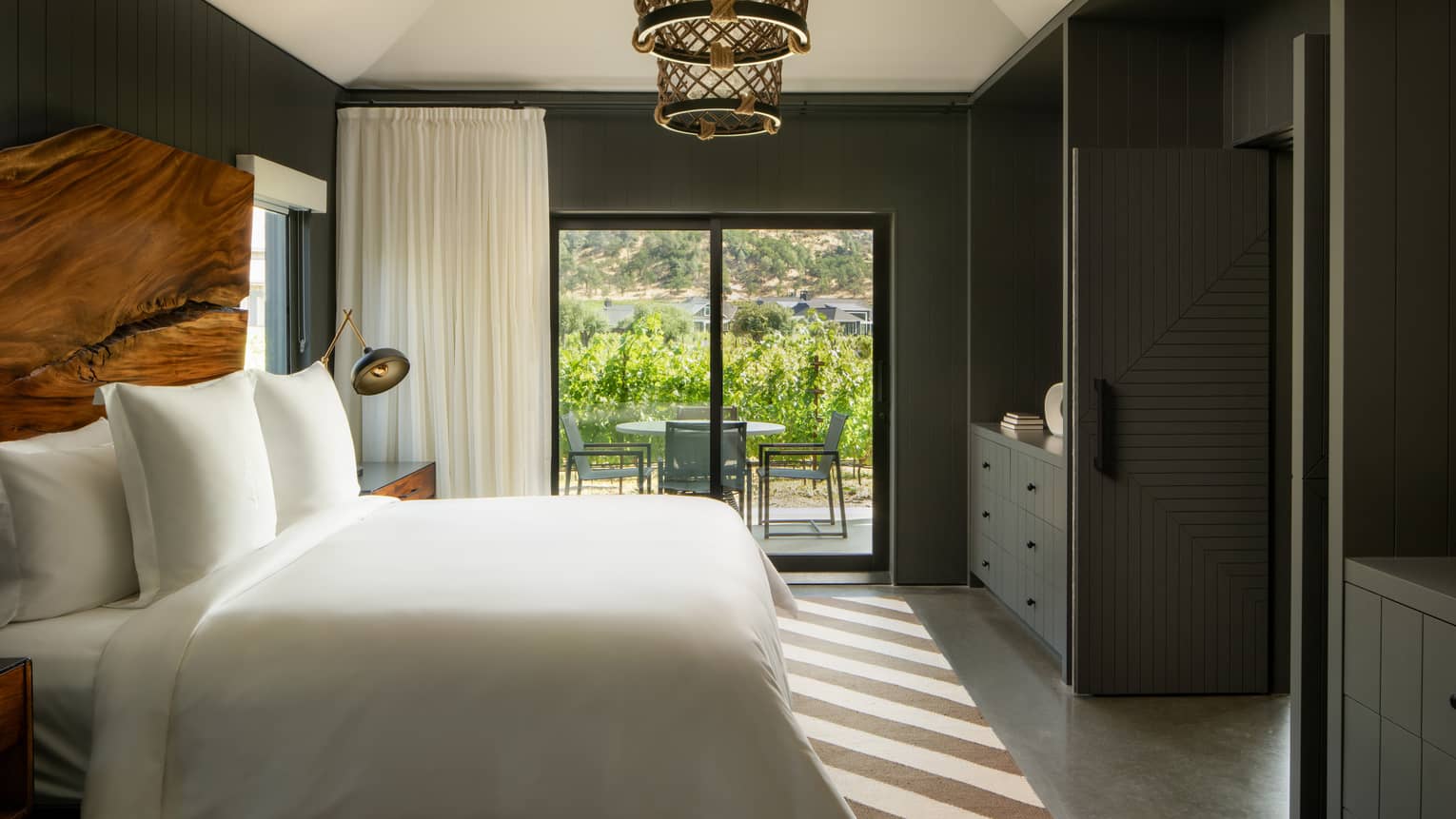 Contemporary bedroom with king bed, diagonal striped rug, natural wood headboard and walk-out terrace