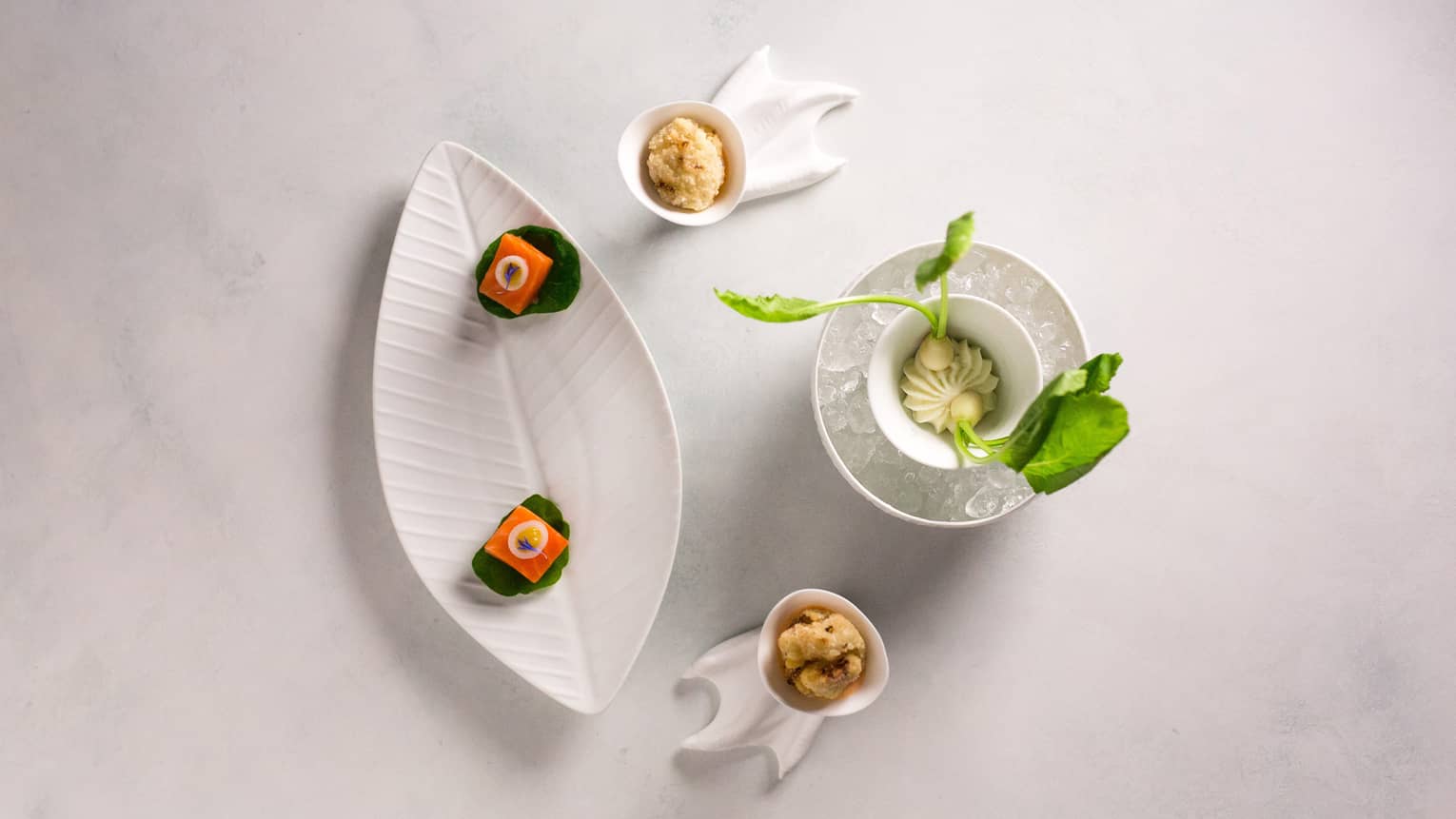 A series of small foods on decorative white plates and bowls.