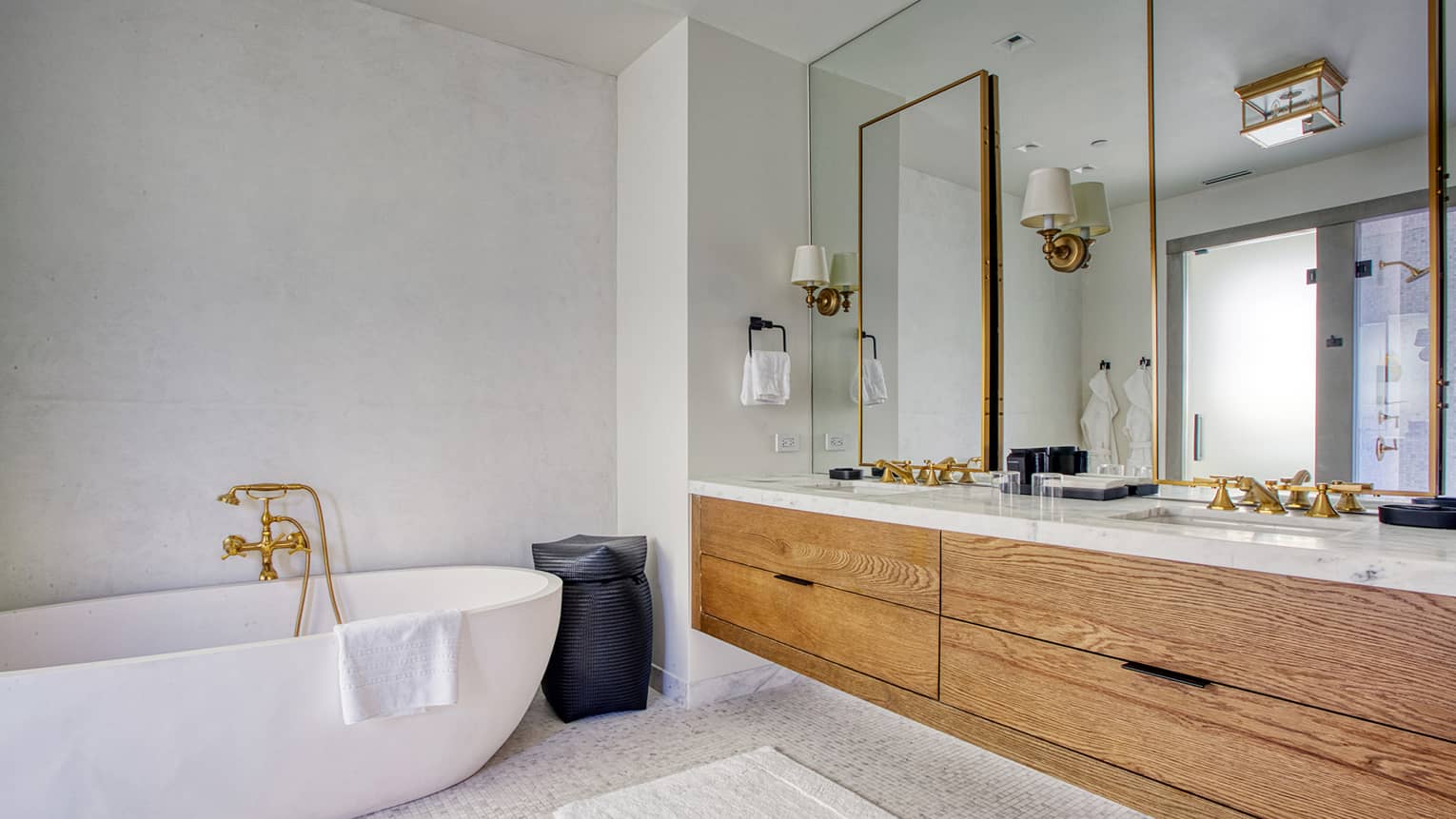 Luxury resort bathroom with a freestanding bathtub, wooden vanity with marble countertop, gold fixtures, mirrors and wall sconces